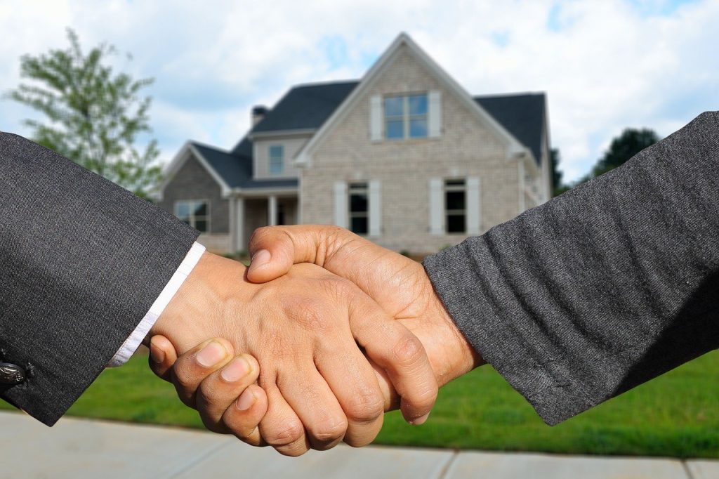 deux personnes qui se serrent la main devant une maison